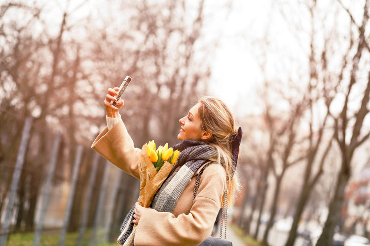 Woman holding mobile phone while standing on tree