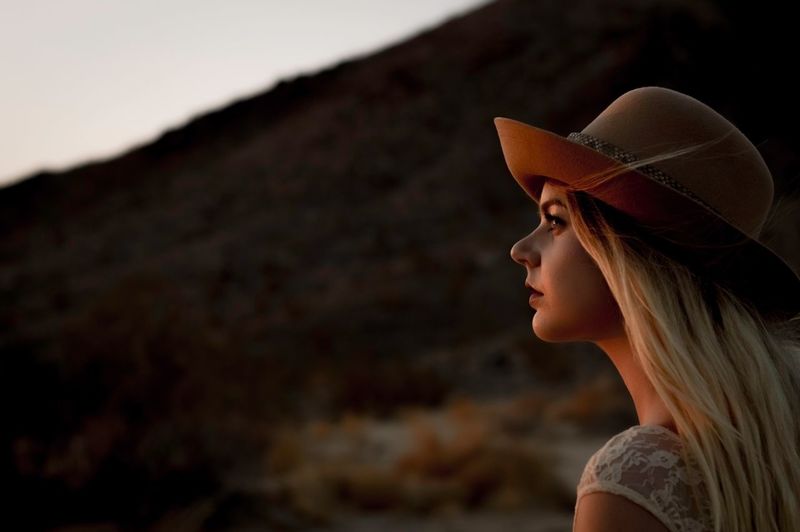 Side view of young woman wearing hat during sunset