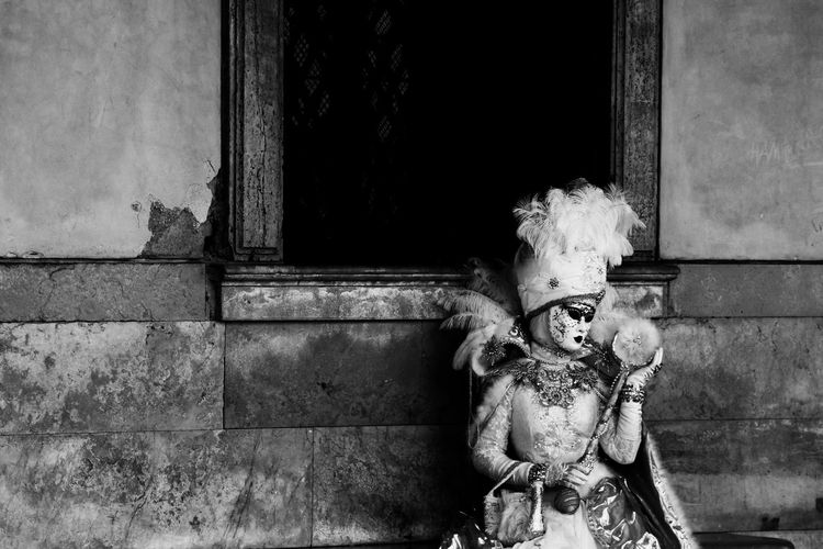 Woman wearing costume and mask standing against old building