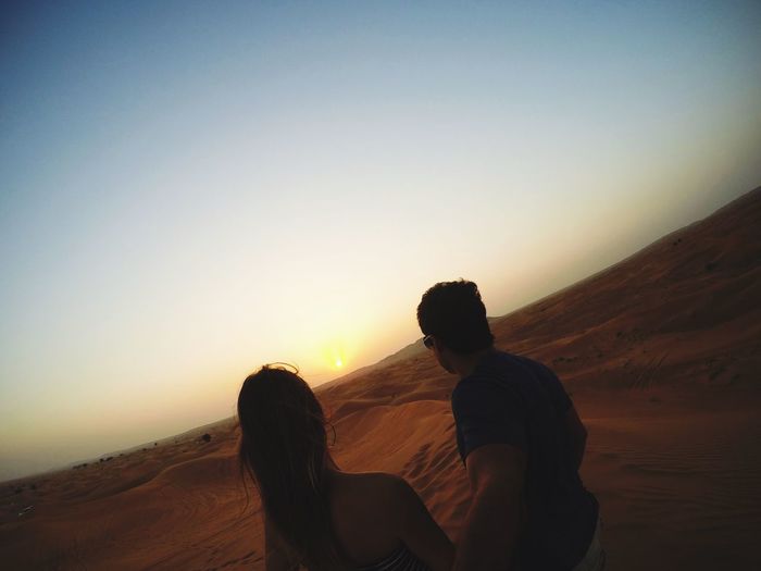 Tilt image of couple standing on desert against sky during sunset