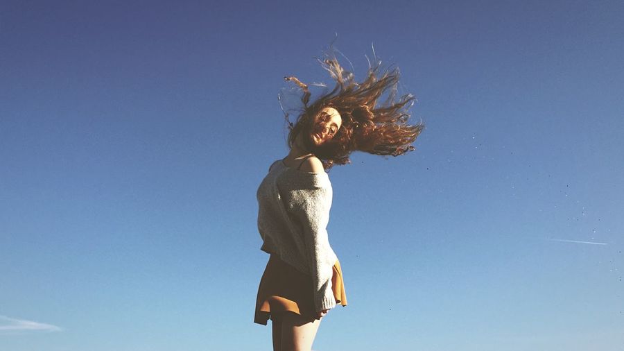 Young woman tossing hair against clear blue sky