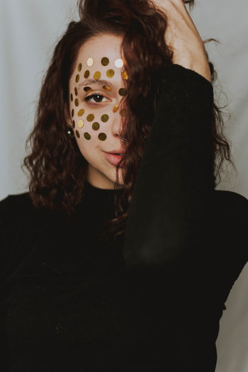 Portrait of young woman with glitter on face standing against gray background