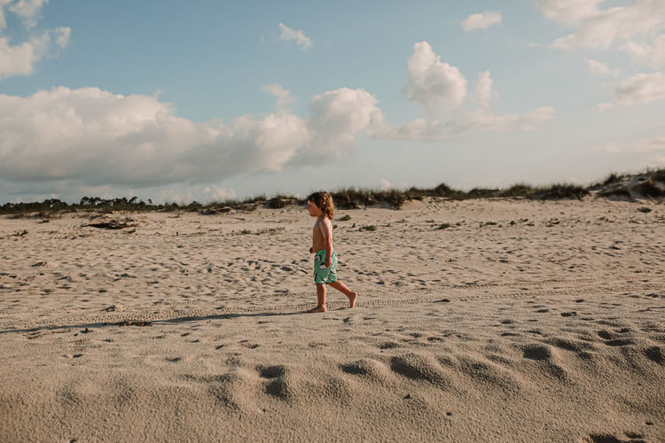 Full length of elementary boy walking on beach against sky