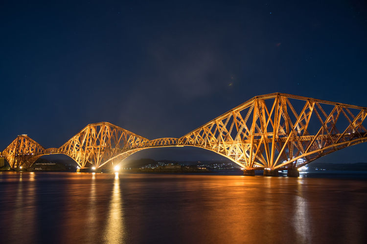 Illuminated firth of forth rail bridge over river at night