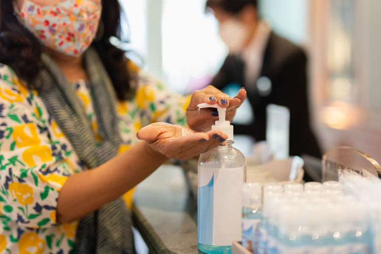 Woman with  protective mask hand pressing alcohol gel at hotel reception.