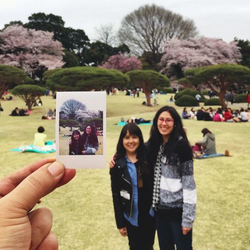 Cropped image of hand holding polaroid against mother and daughter at park