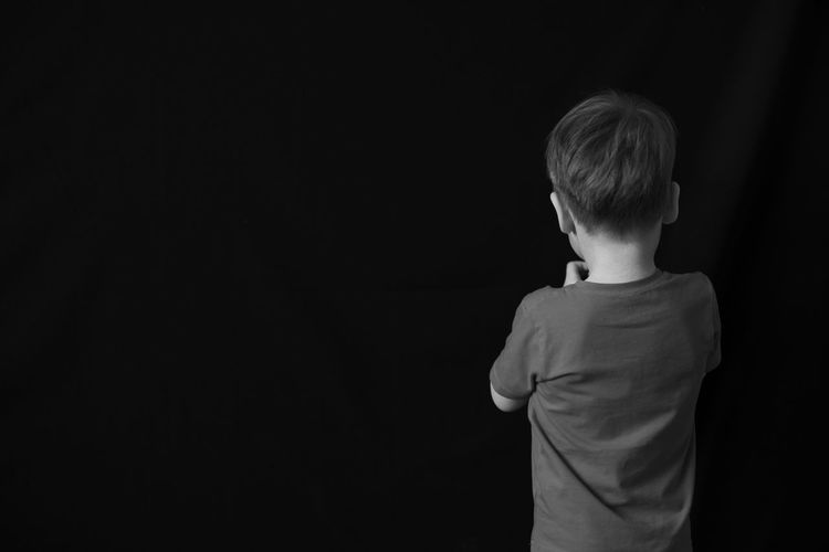 Rear view of boy standing against black background