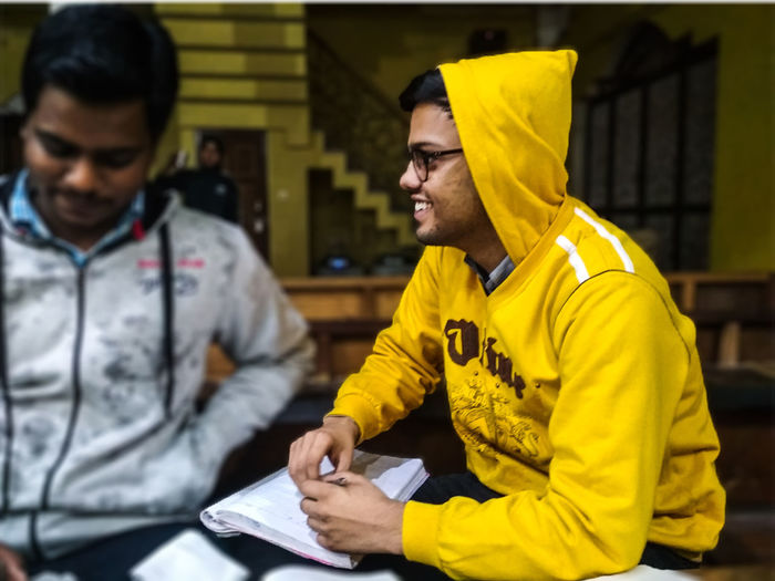 Smiling young man wearing hooded shirt while studying with friend at home