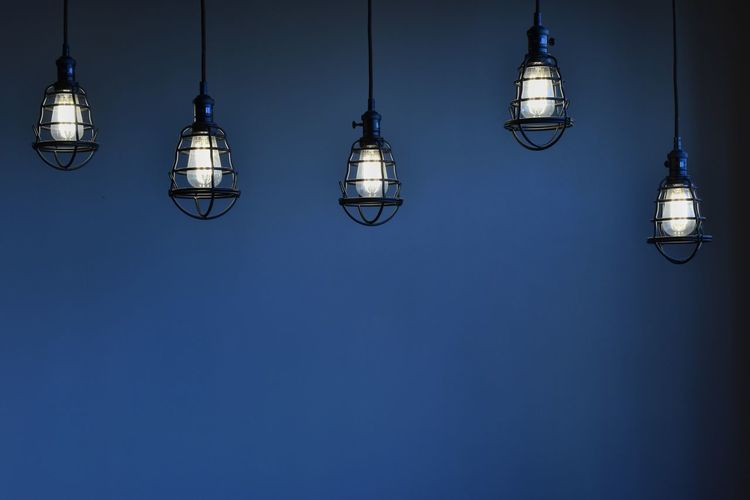 Low angle view of illuminated pendant light against blue sky