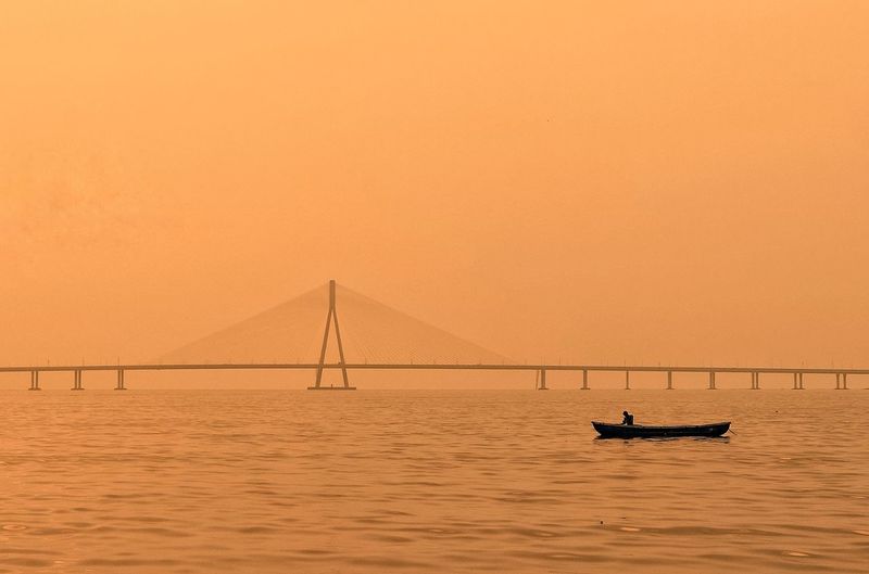 Scenic view of suspension bridge over sea against sky during sunset