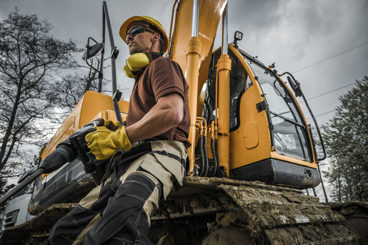 Low angle view of construction worker by excavator