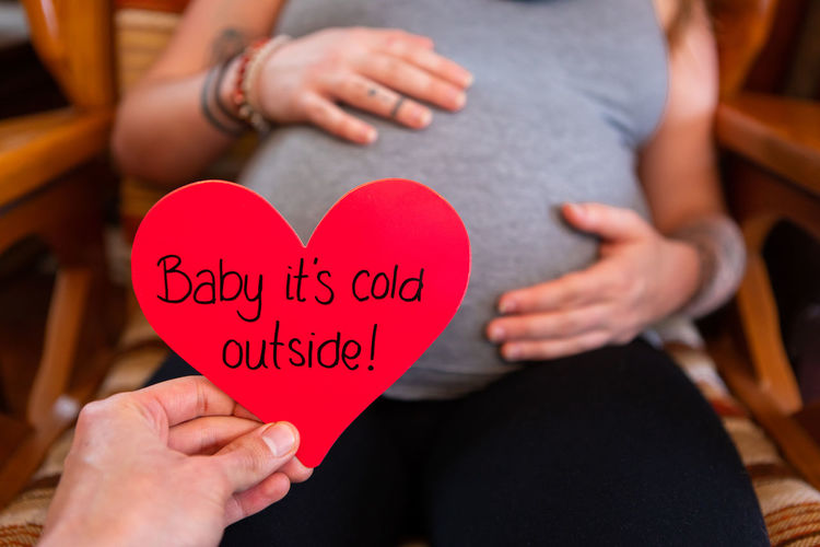 Cropped hand holding heart shape paper against pregnant woman