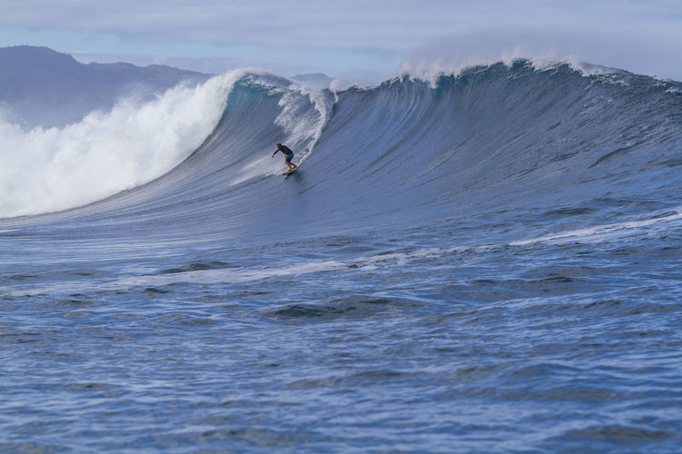 Man surfing on waves at sea against sky