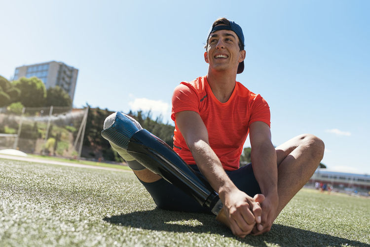 Full length of athlete with prosthetic leg sitting on field against sky