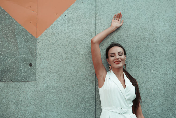 Portrait of a smiling young woman standing against wall