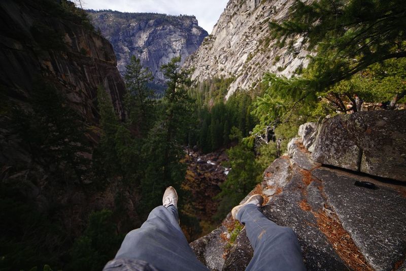 Low section of man sitting on cliff in forest