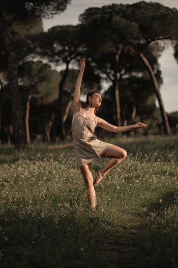 Tranquil female ballet dancer balancing barefoot on meadow in park in iceland while performing with closed eyes and outstretched arms