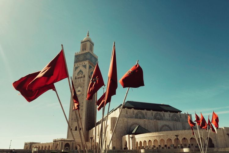 Moroccan flags by mosque hassan ii against sky