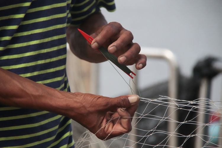 Midsection of man repairing fishing net