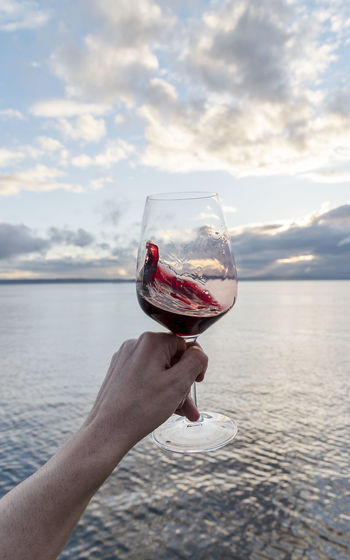 Swirling red wine point of view over sea with dramatic sunset sky, vertical.