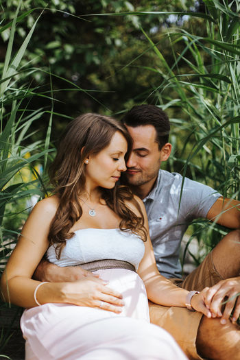 Husband sitting with pregnant wife against plants