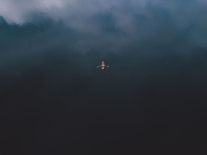 Top view of a orange boat sailing in the dark blue water. view of row boat wih human hands paddling