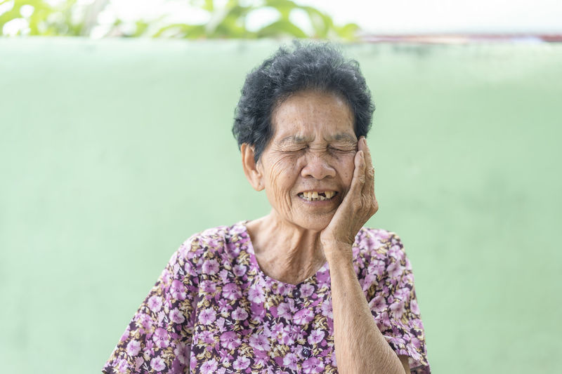 Senior black-haired woman touching the mouth with hand with painful expression because of toothache