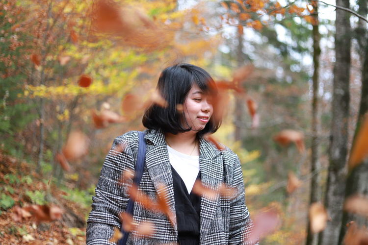 Smiling young woman standing amidst falling leaves during autumn