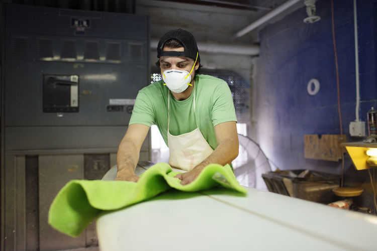 Male worker wiping surfboard with fabric in workshop