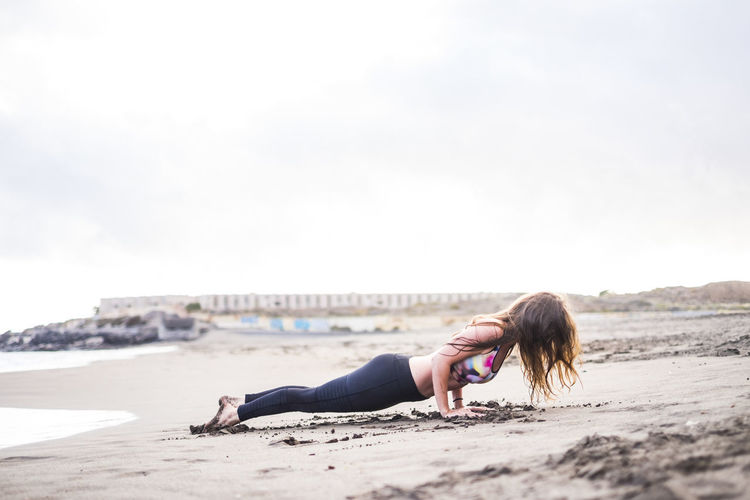 Full length of woman exercising on beach against clear sky