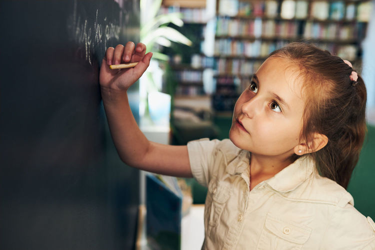 Little girl writing on blackboard. smart student put solve on chalkboard. back to school