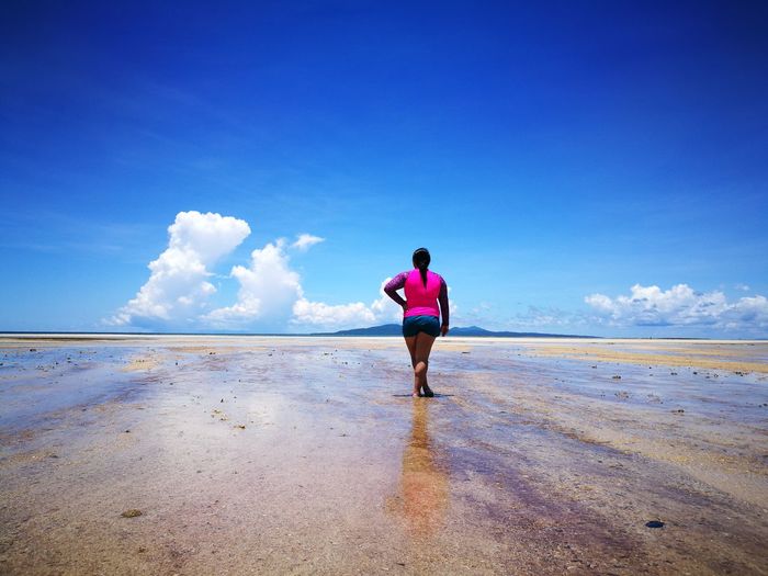Rear view of woman standing on beach against blue sky