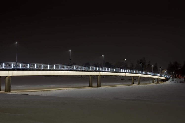 Bridge over illuminated street against clear sky at night