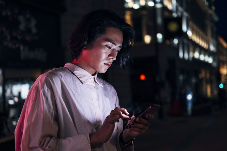 Handsome young man surfing net through mobile phone in city