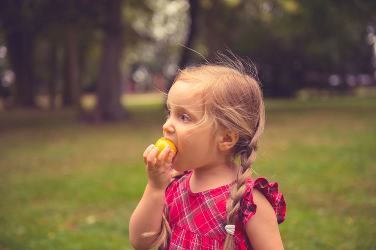Girl eating food while standing on field at public park