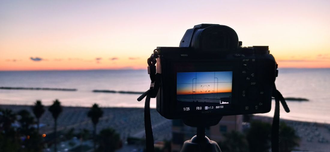 View of camera on beach against sky during sunset