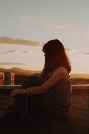 Mature woman sitting on terrace against sky during sunset