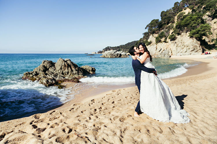 Happy newlywed couple romancing at beach against clear sky