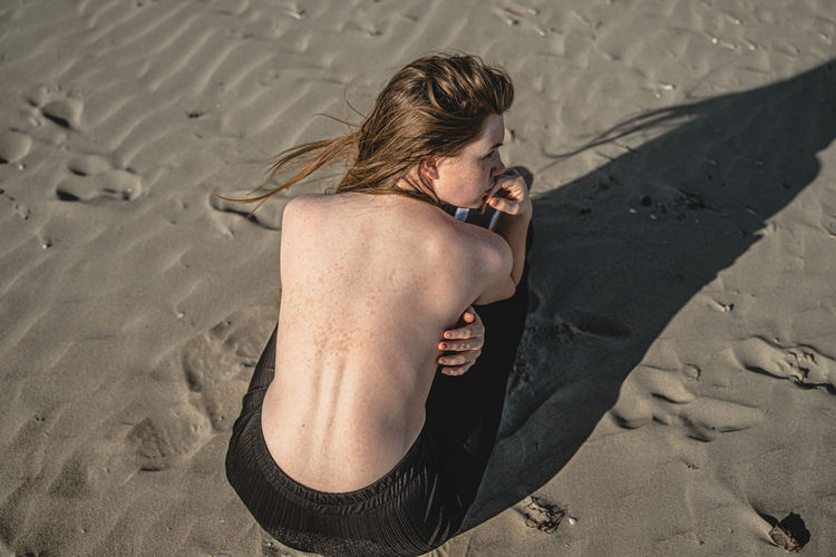 High angle view of shirtless woman crouching on sand
