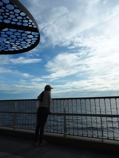 Rear view of woman standing by railing against sea