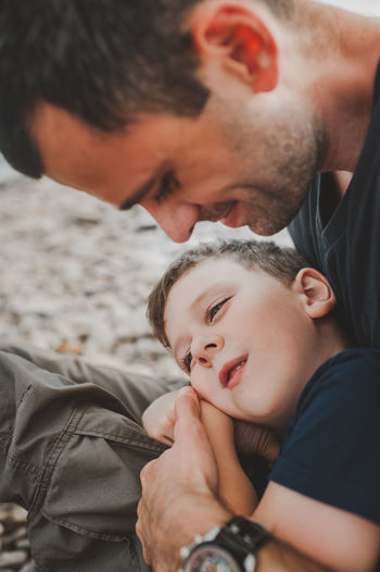 Preschooler boy in a dark blue t-shirt lies in his father's arms and look away