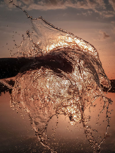Close-up of water splashing on beach against sky during sunset