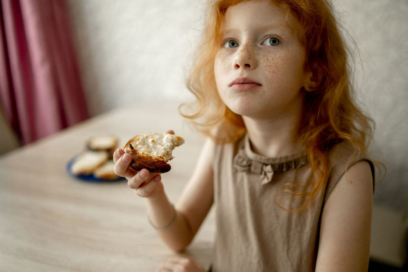 Redhead girl eating cheesecake at table