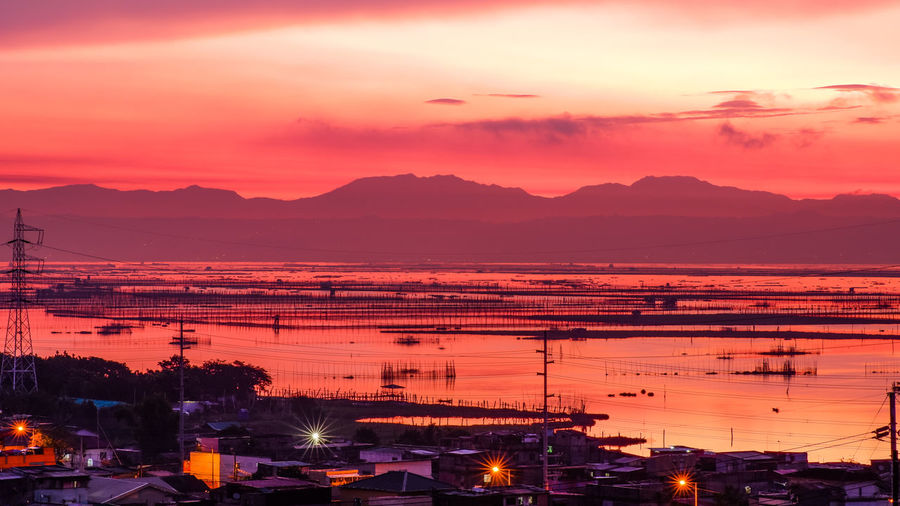 Illuminated city by sea against romantic sky at sunrise