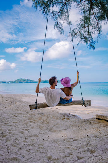 People sitting on swing at beach against sky