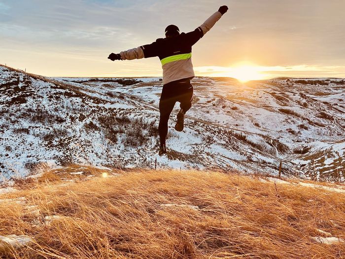 Rear view of man jumping against snow covered landscape during winter