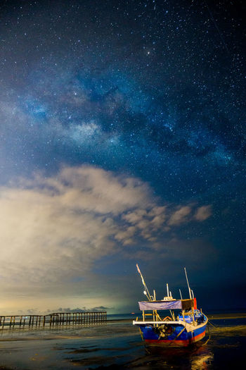 Boat anchored at sea with clouds and stars in sky at dusk