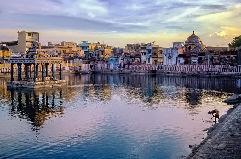 Holy tank of hindu temple with pavilion against background of houses at sunset. 