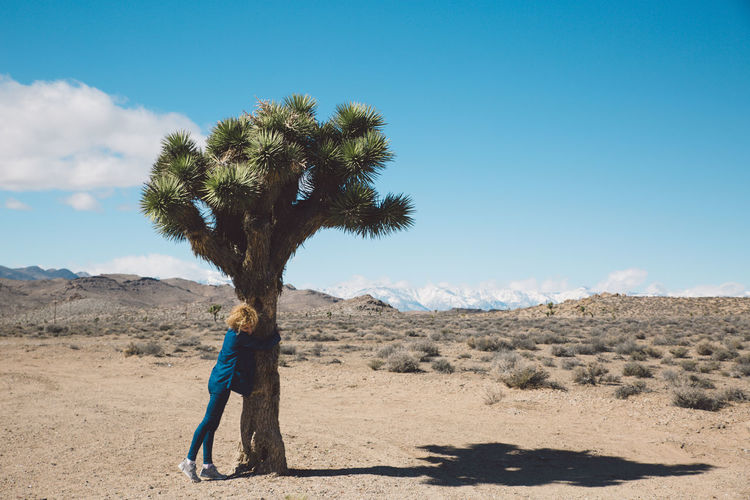 Woman hugging tree in desert against sky