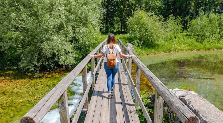 Rear view of young woman standing on footbridge over creek.
